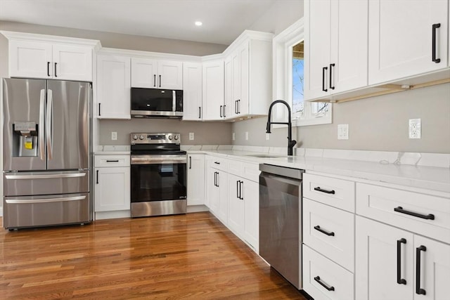 kitchen with sink, dark wood-type flooring, appliances with stainless steel finishes, white cabinetry, and light stone counters