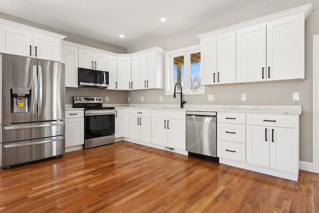 kitchen with sink, white cabinets, stainless steel appliances, light stone countertops, and dark wood-type flooring