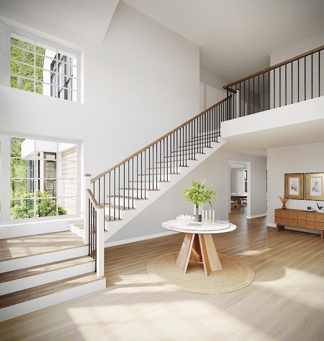 staircase featuring baseboards, a high ceiling, a wealth of natural light, and wood finished floors
