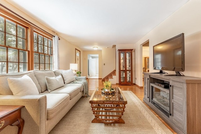 living area with light wood finished floors, stairway, and a glass covered fireplace