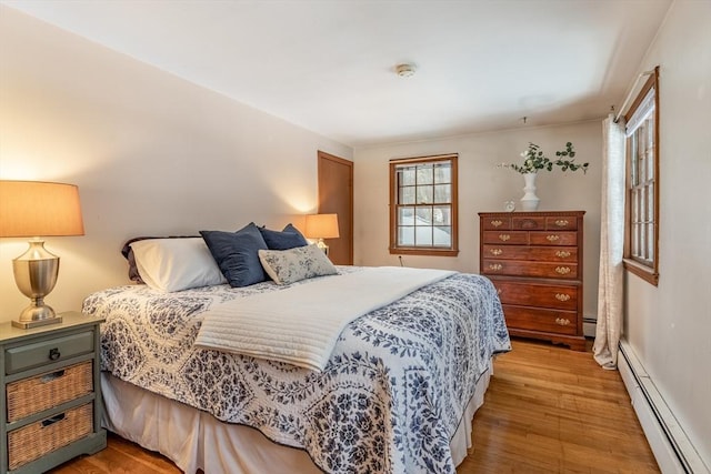 bedroom with a baseboard heating unit and light wood finished floors