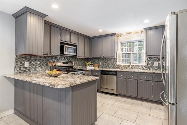 kitchen featuring light tile patterned floors, stainless steel appliances, decorative backsplash, a sink, and a peninsula