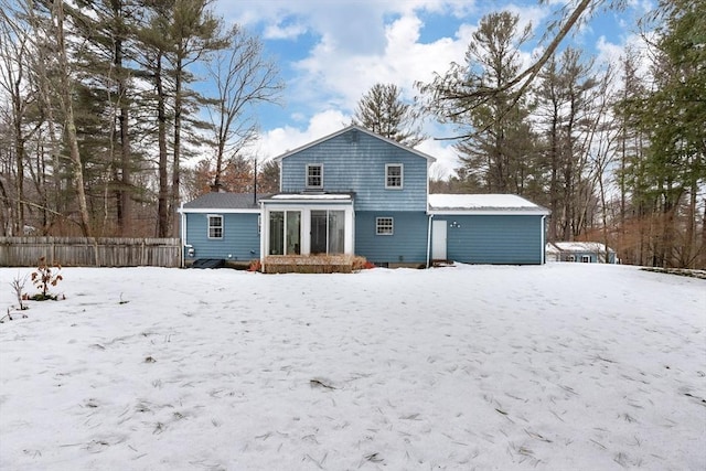 snow covered rear of property featuring a sunroom and fence