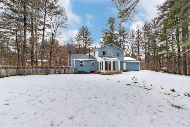 snow covered rear of property with a detached garage and fence