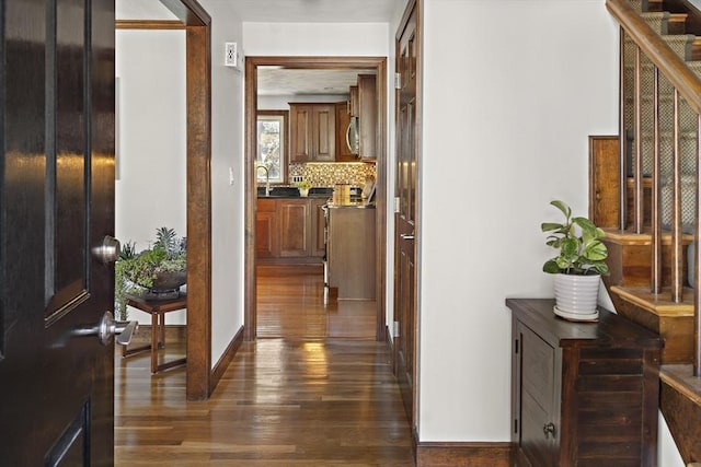 hall with dark wood-type flooring, baseboards, and a sink