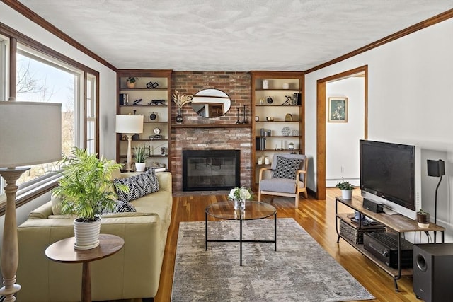 living area with built in shelves, ornamental molding, a textured ceiling, wood finished floors, and a brick fireplace