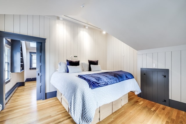 bedroom with a baseboard radiator, light wood-type flooring, track lighting, and lofted ceiling