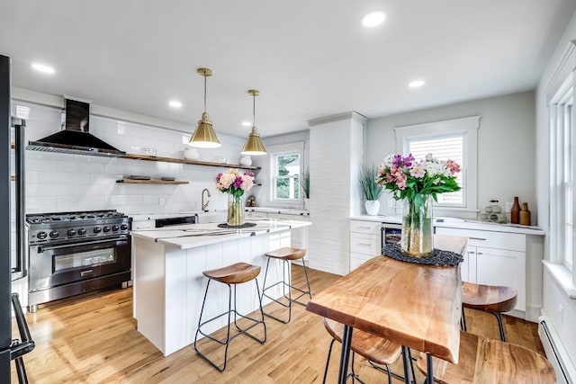 kitchen with decorative backsplash, wall chimney range hood, high end black range, light wood-type flooring, and a baseboard heating unit