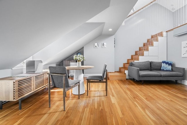 dining area featuring lofted ceiling, stairs, wood finished floors, and an AC wall unit