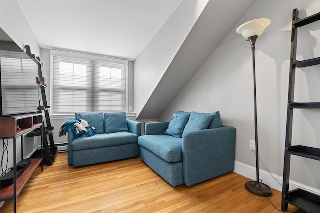 living area with a baseboard heating unit, light wood-type flooring, and baseboards