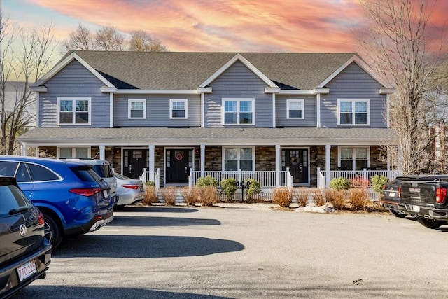 townhome / multi-family property with stone siding, a porch, and a shingled roof