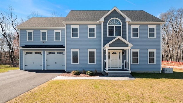 colonial house with driveway, an attached garage, a shingled roof, and a front yard