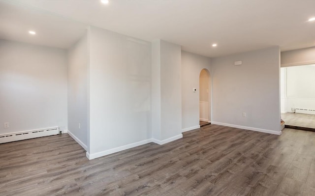 spare room featuring arched walkways, a baseboard heating unit, wood finished floors, and recessed lighting