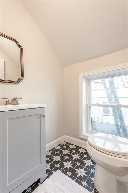 half bathroom with toilet, vaulted ceiling, vanity, baseboards, and tile patterned floors