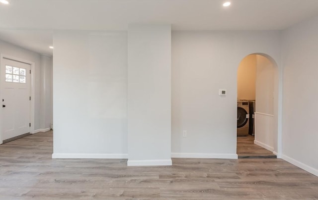 spare room with light wood-type flooring, arched walkways, washer / clothes dryer, and baseboards