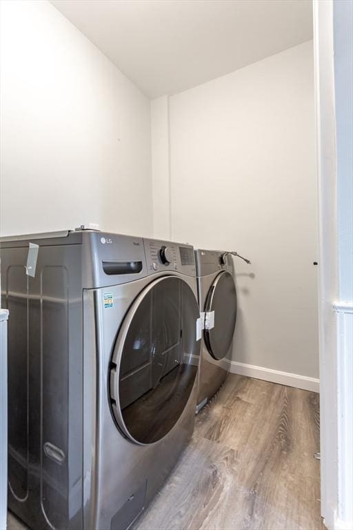 clothes washing area featuring laundry area, washing machine and dryer, baseboards, and wood finished floors