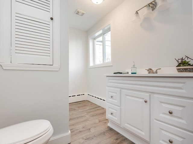 bathroom with visible vents, toilet, wood finished floors, vanity, and a baseboard heating unit