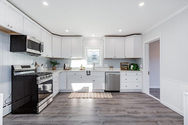 kitchen featuring crown molding, white cabinetry, stainless steel appliances, and wood finished floors