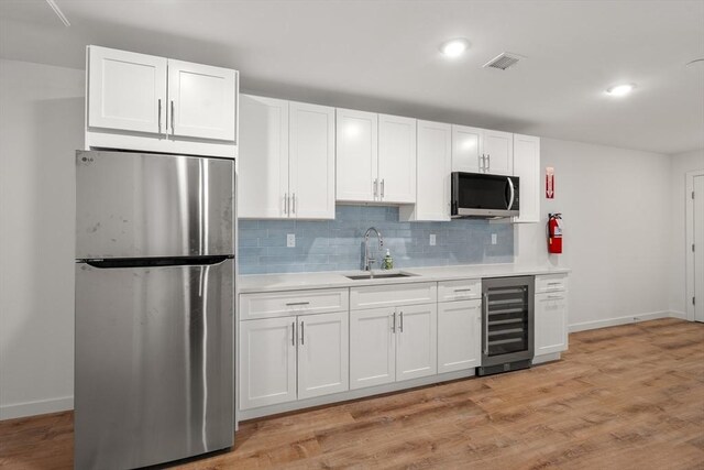 kitchen with a sink, light countertops, white cabinets, wine cooler, and stainless steel appliances