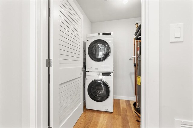 washroom with stacked washer / drying machine, light wood finished floors, and laundry area