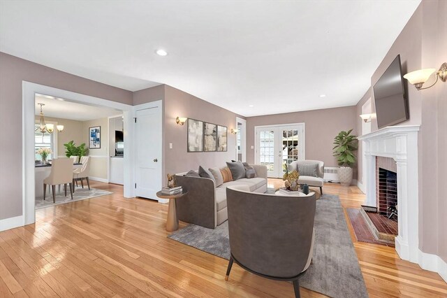 living area with a fireplace with flush hearth, light wood-style flooring, recessed lighting, an inviting chandelier, and baseboards