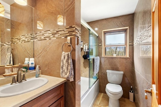 bathroom featuring tile walls, toilet, vanity, and combined bath / shower with glass door