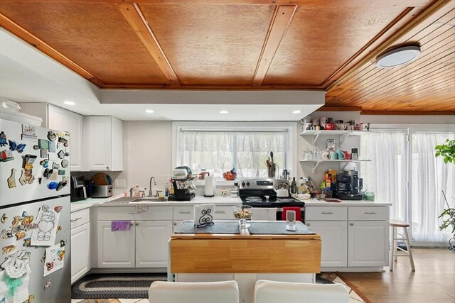 kitchen with freestanding refrigerator, stainless steel range with electric stovetop, wooden ceiling, white cabinetry, and light countertops