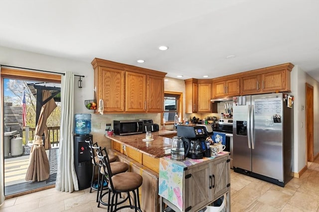 kitchen with appliances with stainless steel finishes, under cabinet range hood, brown cabinetry, recessed lighting, and a breakfast bar