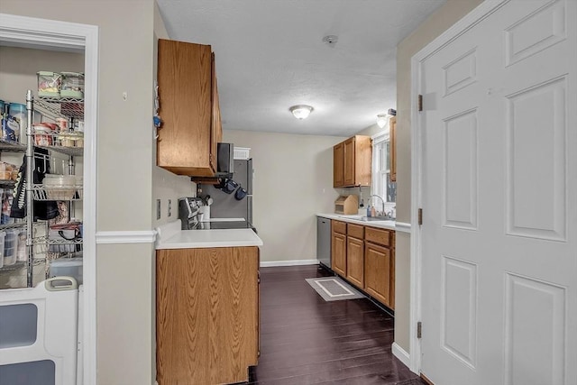 kitchen with appliances with stainless steel finishes, dark hardwood / wood-style flooring, washer / clothes dryer, and sink