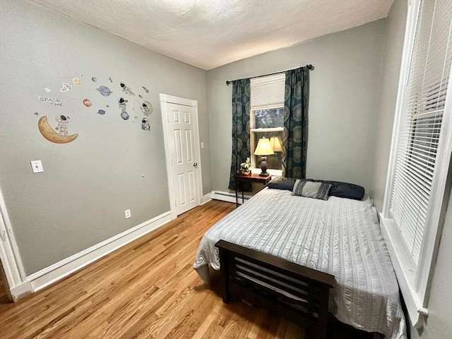 bedroom featuring baseboard heating, light wood-style floors, and baseboards