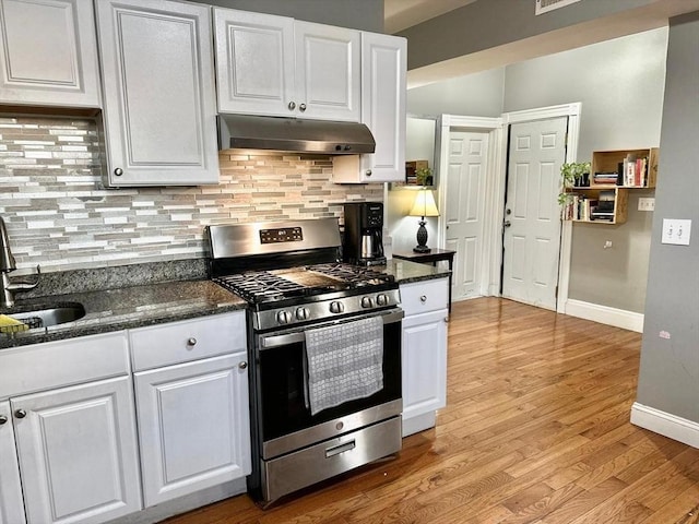 kitchen with gas range, under cabinet range hood, white cabinetry, a sink, and baseboards