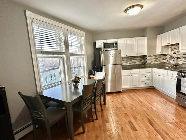 kitchen featuring appliances with stainless steel finishes, a sink, a baseboard heating unit, dark countertops, and decorative backsplash