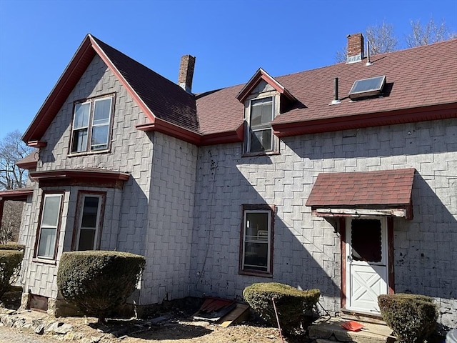 exterior space with roof with shingles and a chimney