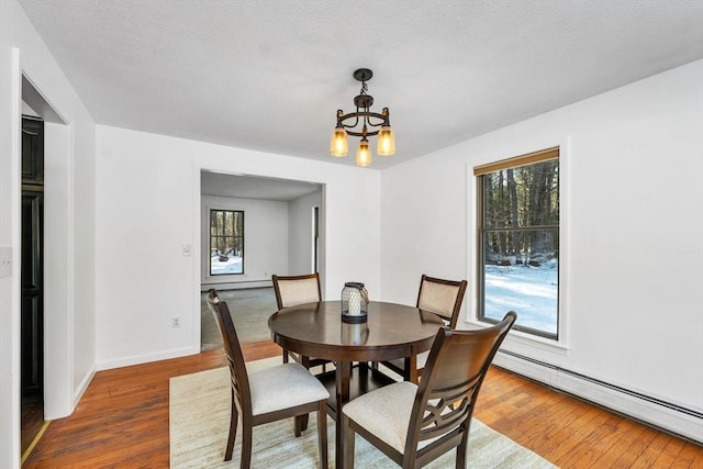 dining room with baseboard heating, a healthy amount of sunlight, an inviting chandelier, and hardwood / wood-style flooring