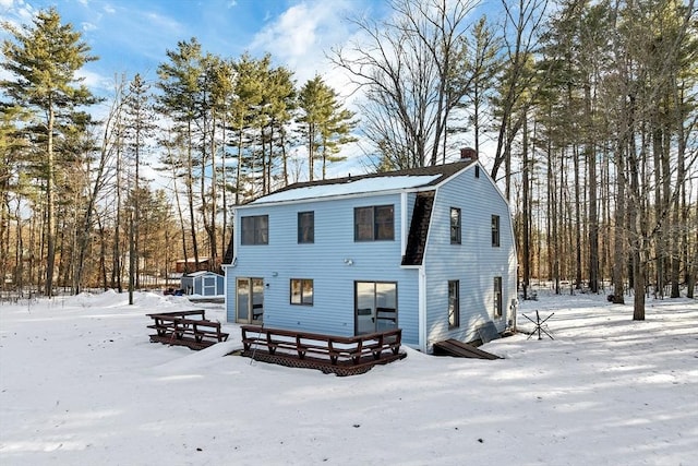 view of front of home with a gambrel roof, an outbuilding, a deck, and a chimney