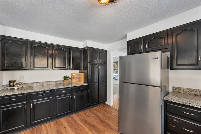 kitchen with a textured ceiling, light wood-style floors, dark cabinetry, and freestanding refrigerator