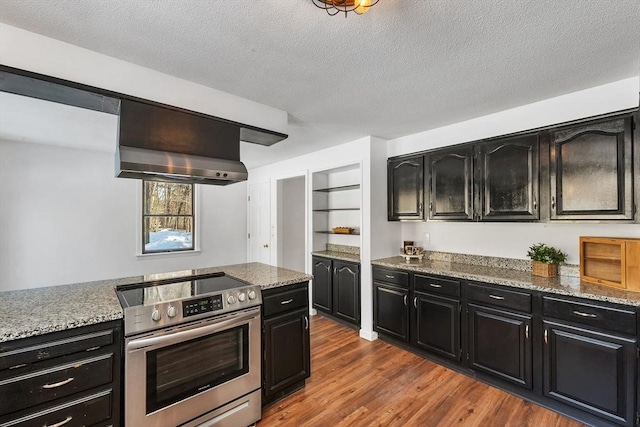 kitchen featuring ventilation hood, stainless steel range with electric cooktop, dark cabinetry, a textured ceiling, and dark wood-style flooring