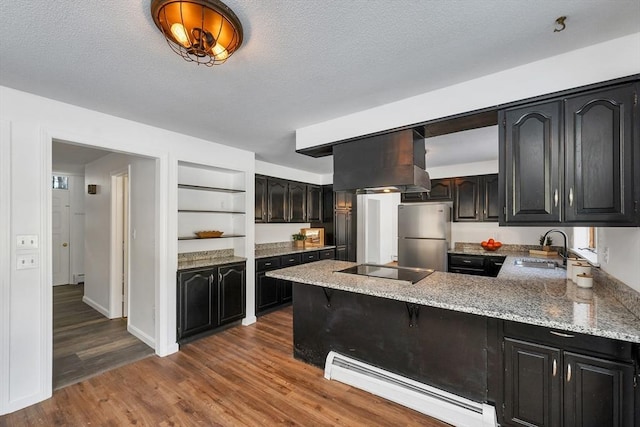 kitchen with baseboard heating, range hood, a peninsula, freestanding refrigerator, and a sink