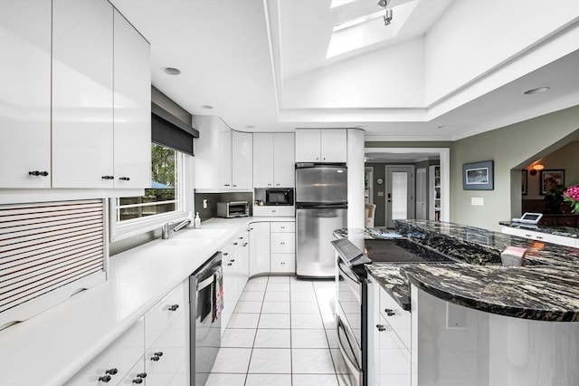 64 Pond St, Nahant, MA 01908 - kitchen featuring appliances with stainless steel finishes, white cabinets, light tile patterned floors, dark stone counters, and vaulted ceiling