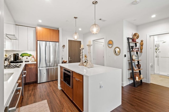 kitchen with pendant lighting, stainless steel appliances, dark hardwood / wood-style floors, a center island, and white cabinets