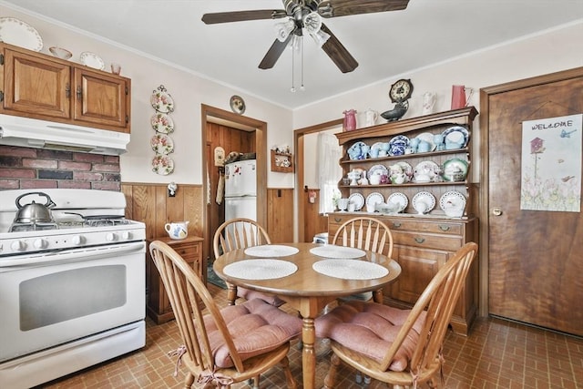 dining area with brick patterned flooring, a wainscoted wall, ceiling fan, crown molding, and wood walls