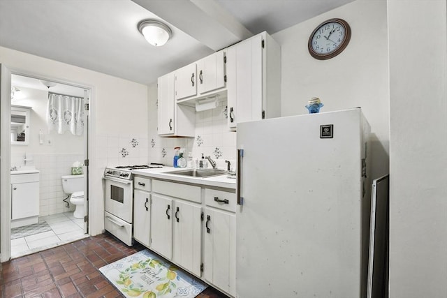 kitchen featuring a sink, white appliances, white cabinets, tile walls, and light countertops