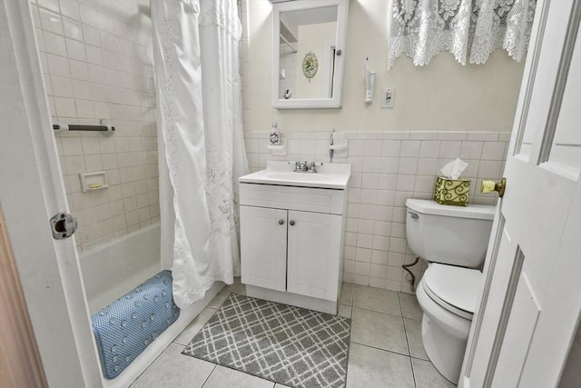 bathroom featuring toilet, tile patterned flooring, tile walls, vanity, and wainscoting