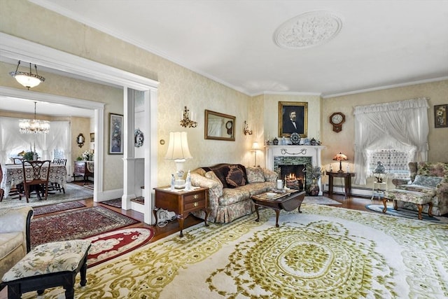 living area featuring wood finished floors, a chandelier, a lit fireplace, baseboard heating, and ornamental molding