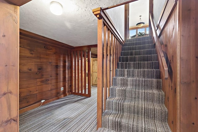 stairway featuring carpet flooring, wooden walls, and a textured ceiling