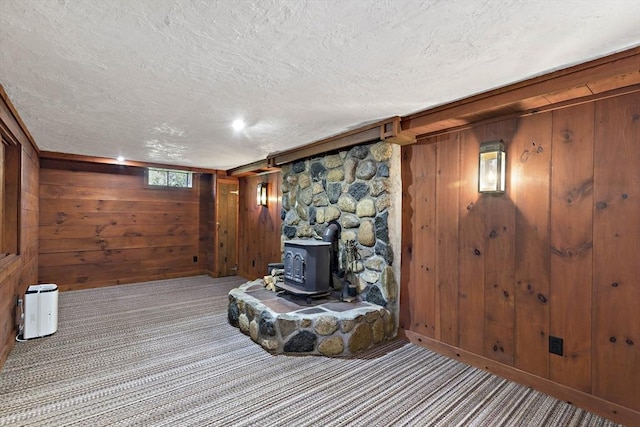 living area with a wood stove, wooden walls, a textured ceiling, and carpet