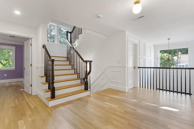 stairs featuring wood-type flooring, a chandelier, and a healthy amount of sunlight