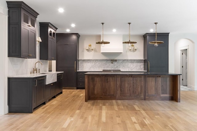 kitchen with light hardwood / wood-style floors, hanging light fixtures, a center island, decorative backsplash, and dark brown cabinetry