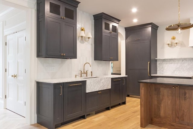 kitchen with sink, light stone counters, light hardwood / wood-style flooring, decorative backsplash, and pendant lighting