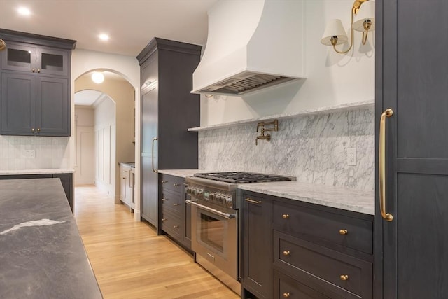 kitchen featuring light stone counters, light wood-type flooring, backsplash, premium range hood, and high quality appliances